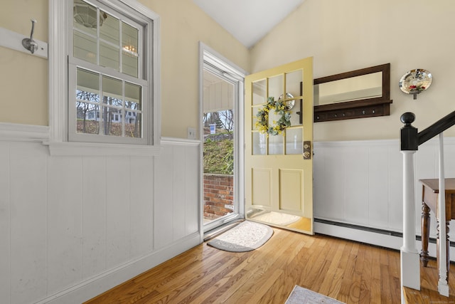 foyer entrance with vaulted ceiling, wood finished floors, a decorative wall, and a wainscoted wall