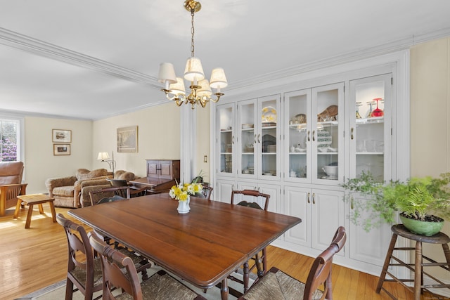 dining area with ornamental molding, a notable chandelier, and light wood finished floors