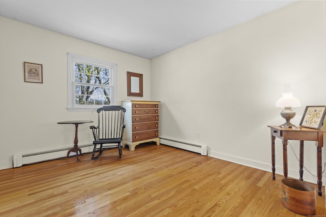 living area with a baseboard heating unit, light wood finished floors, and baseboards