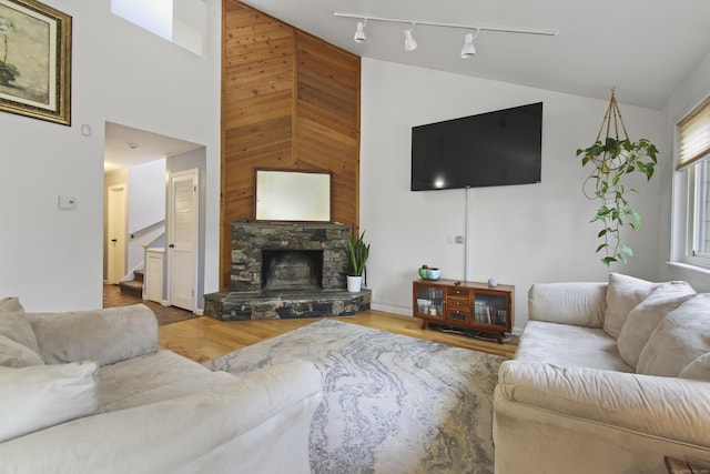 living area featuring stairway, high vaulted ceiling, track lighting, a stone fireplace, and wood finished floors