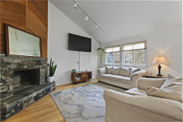 living room with track lighting, a stone fireplace, vaulted ceiling, baseboards, and wood finished floors