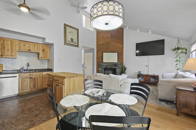 dining space featuring high vaulted ceiling, a stone fireplace, ceiling fan, and light wood-type flooring