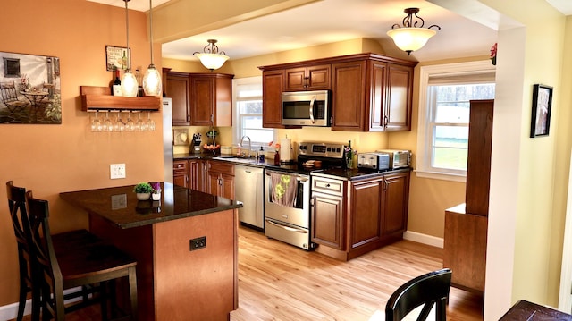 kitchen with a sink, light wood-style floors, a breakfast bar, a peninsula, and appliances with stainless steel finishes