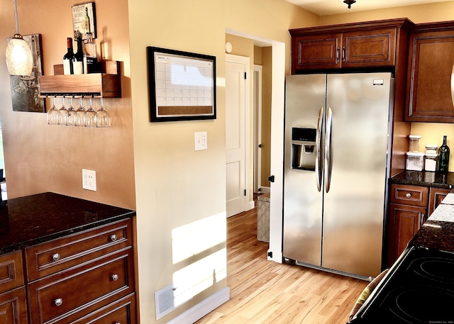 kitchen featuring dark stone counters, decorative light fixtures, stainless steel fridge, light wood finished floors, and visible vents