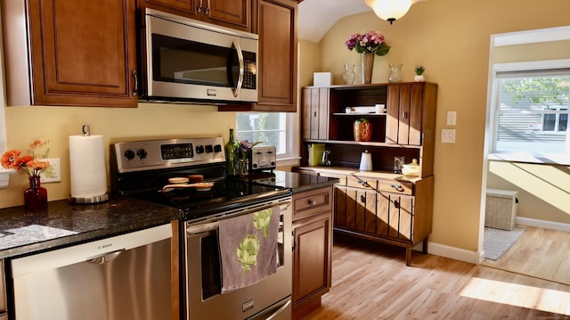 kitchen with dark stone counters, stainless steel appliances, open shelves, brown cabinetry, and light wood-type flooring