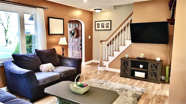 living area featuring baseboards, arched walkways, stairs, and light wood finished floors
