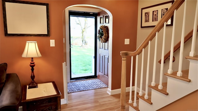 entryway with baseboards, arched walkways, wood finished floors, and plenty of natural light