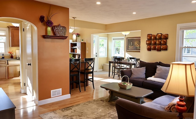 living area with visible vents, recessed lighting, light wood finished floors, and arched walkways