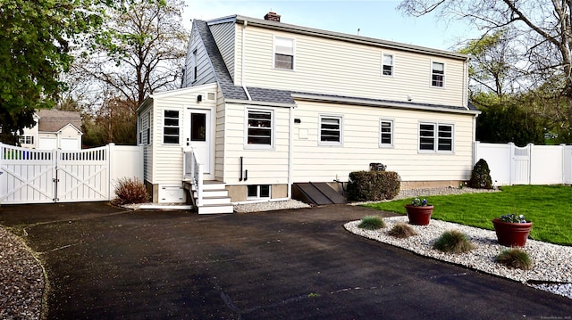 rear view of property with a shingled roof, a gate, a chimney, entry steps, and fence