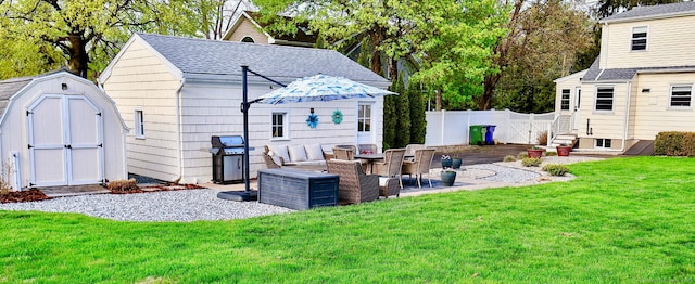 back of property with a yard, fence, an outbuilding, a patio, and roof with shingles