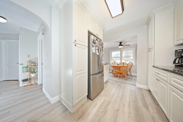 corridor featuring arched walkways, light wood finished floors, and baseboards