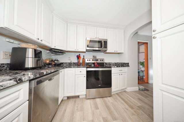 kitchen with light wood finished floors, arched walkways, dark stone countertops, white cabinetry, and appliances with stainless steel finishes
