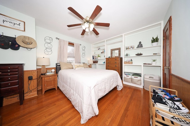 bedroom featuring wooden walls, wood finished floors, and a wainscoted wall