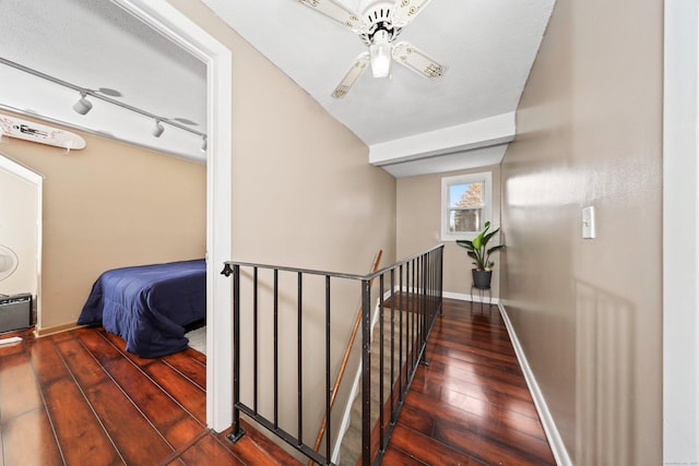 hallway featuring hardwood / wood-style flooring, baseboards, track lighting, and an upstairs landing