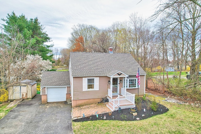 view of front of house with a storage shed, aphalt driveway, an attached garage, an outbuilding, and roof with shingles