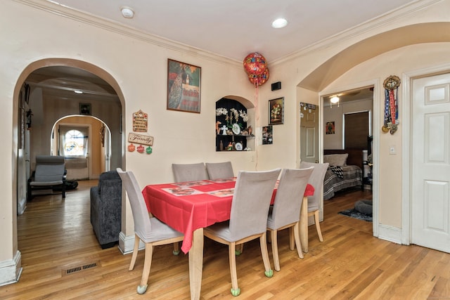 dining area with arched walkways, wood finished floors, visible vents, and ornamental molding