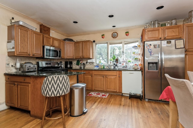 kitchen with light wood finished floors, a sink, crown molding, a peninsula, and appliances with stainless steel finishes