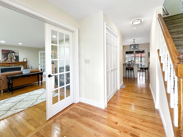 corridor with an inviting chandelier, french doors, baseboards, light wood-style floors, and stairs
