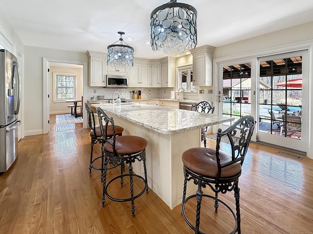 kitchen featuring a kitchen breakfast bar, stainless steel appliances, light wood finished floors, and visible vents
