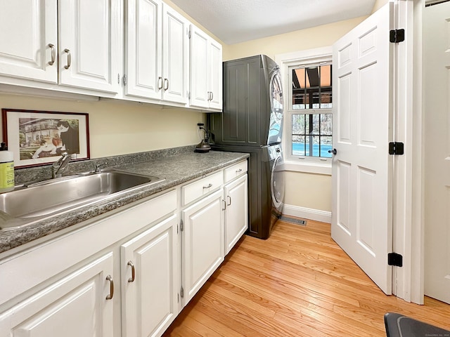 laundry room with cabinet space, a sink, baseboards, light wood finished floors, and stacked washer and clothes dryer