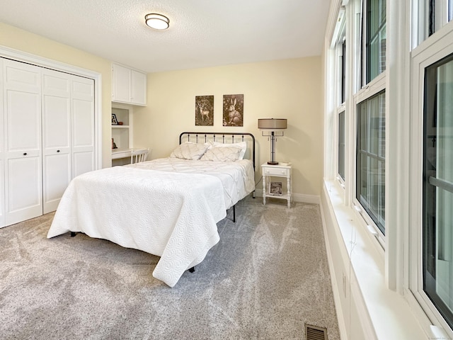 bedroom featuring a closet, carpet flooring, a textured ceiling, and visible vents