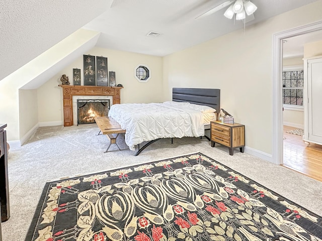 bedroom featuring visible vents, carpet floors, a lit fireplace, a ceiling fan, and vaulted ceiling
