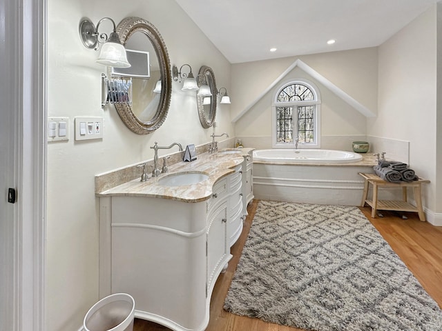 bathroom with a sink, double vanity, a bath, and wood finished floors
