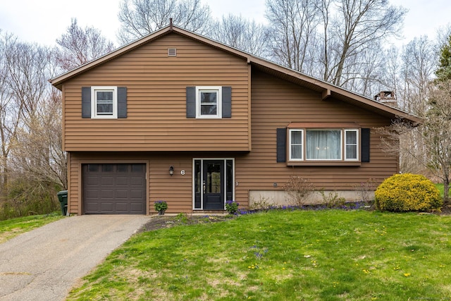 split level home featuring a chimney, an attached garage, driveway, and a front lawn