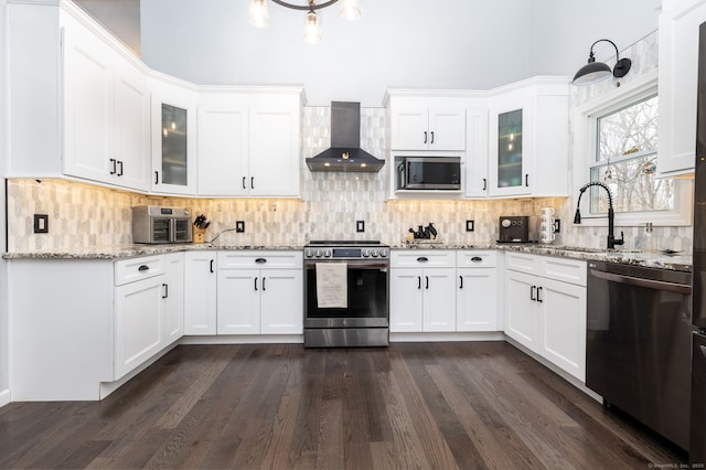 kitchen featuring wall chimney exhaust hood, a sink, white cabinetry, and appliances with stainless steel finishes