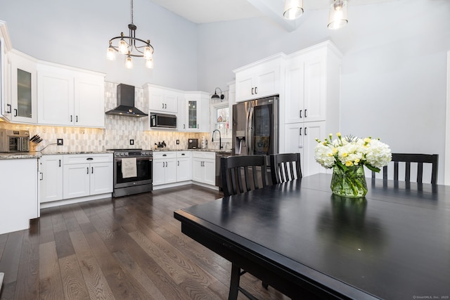 kitchen with a chandelier, decorative backsplash, wall chimney range hood, high vaulted ceiling, and appliances with stainless steel finishes