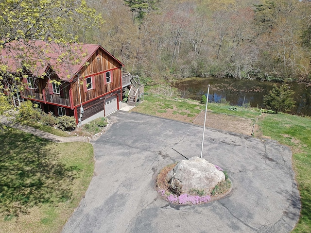 view of home's exterior featuring stairs, aphalt driveway, a garage, a water view, and a wooded view