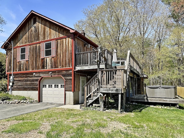 back of house with aphalt driveway, a deck, an attached garage, a hot tub, and a yard