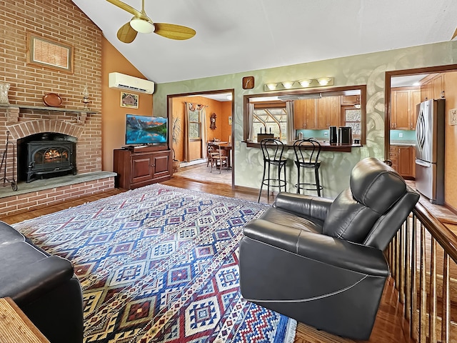 living room with ceiling fan, a wood stove, wood finished floors, vaulted ceiling, and a wall mounted AC