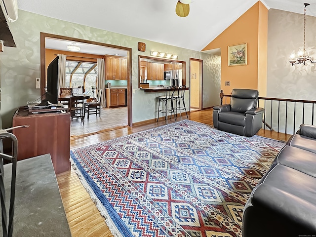 living room with baseboards, light wood-style flooring, a notable chandelier, and vaulted ceiling
