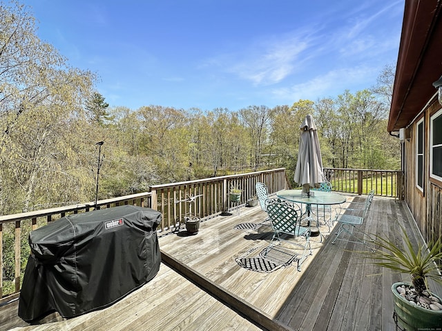 wooden terrace featuring outdoor dining area, grilling area, and a forest view