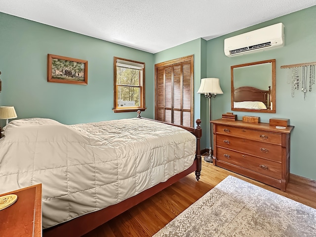 bedroom with a wall unit AC, a textured ceiling, wood finished floors, baseboards, and a closet