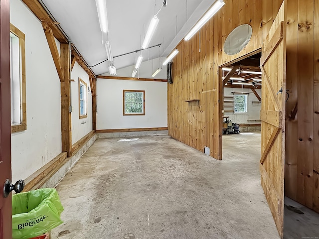 empty room with wood walls, lofted ceiling, and unfinished concrete floors