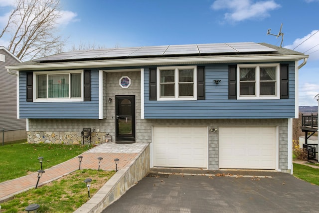 split foyer home featuring an attached garage, aphalt driveway, and solar panels