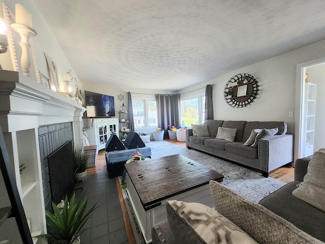 living area with a brick fireplace, a textured ceiling, and wood finished floors