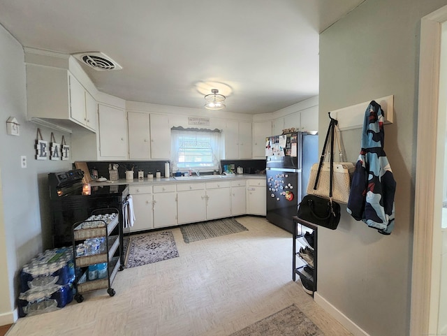 kitchen featuring visible vents, black electric range oven, light countertops, white cabinets, and freestanding refrigerator