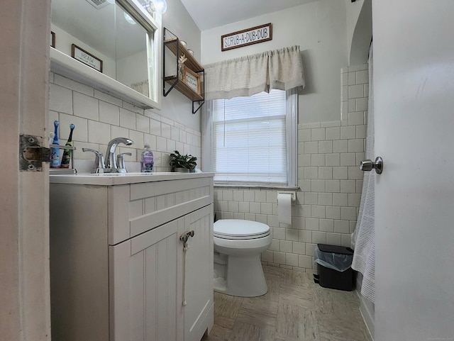 bathroom with vanity, wainscoting, toilet, and tile walls