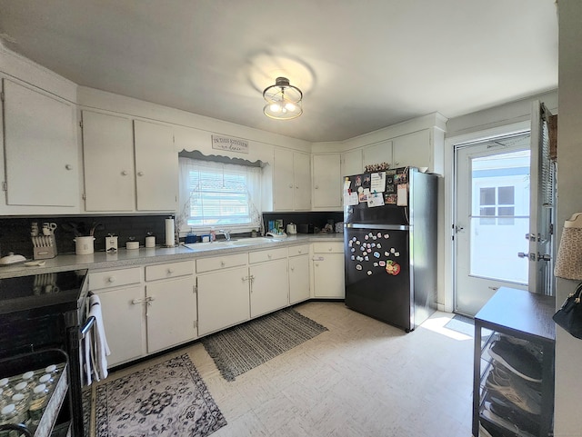 kitchen featuring stainless steel range with electric cooktop, a sink, light countertops, freestanding refrigerator, and light floors