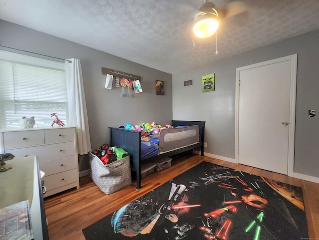 bedroom with a textured ceiling, baseboards, visible vents, and wood finished floors
