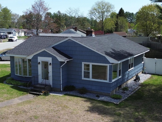 view of front of home with a front lawn, roof with shingles, and fence