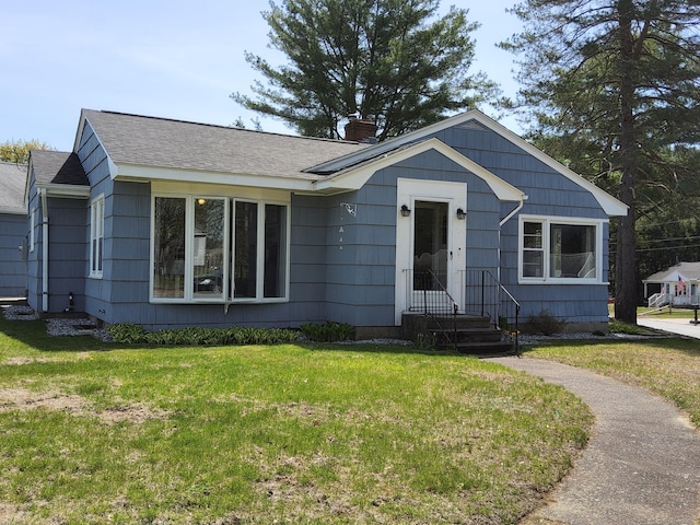 view of front facade with a chimney, a shingled roof, and a front yard
