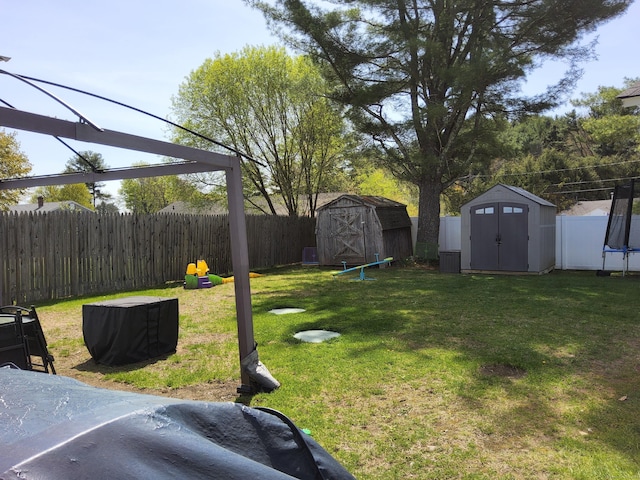 view of yard featuring a fenced backyard, a trampoline, a shed, and an outbuilding
