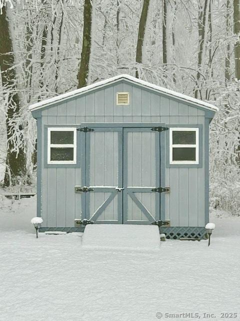 snow covered structure featuring a storage unit and an outdoor structure