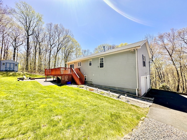 rear view of house featuring driveway, a deck, an outdoor structure, a yard, and an attached garage