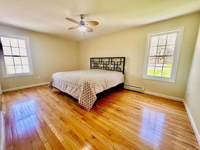 bedroom featuring baseboards, multiple windows, baseboard heating, and light wood-type flooring