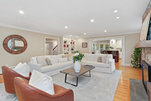 living area with a fireplace with flush hearth, crown molding, light wood-style flooring, recessed lighting, and stairs